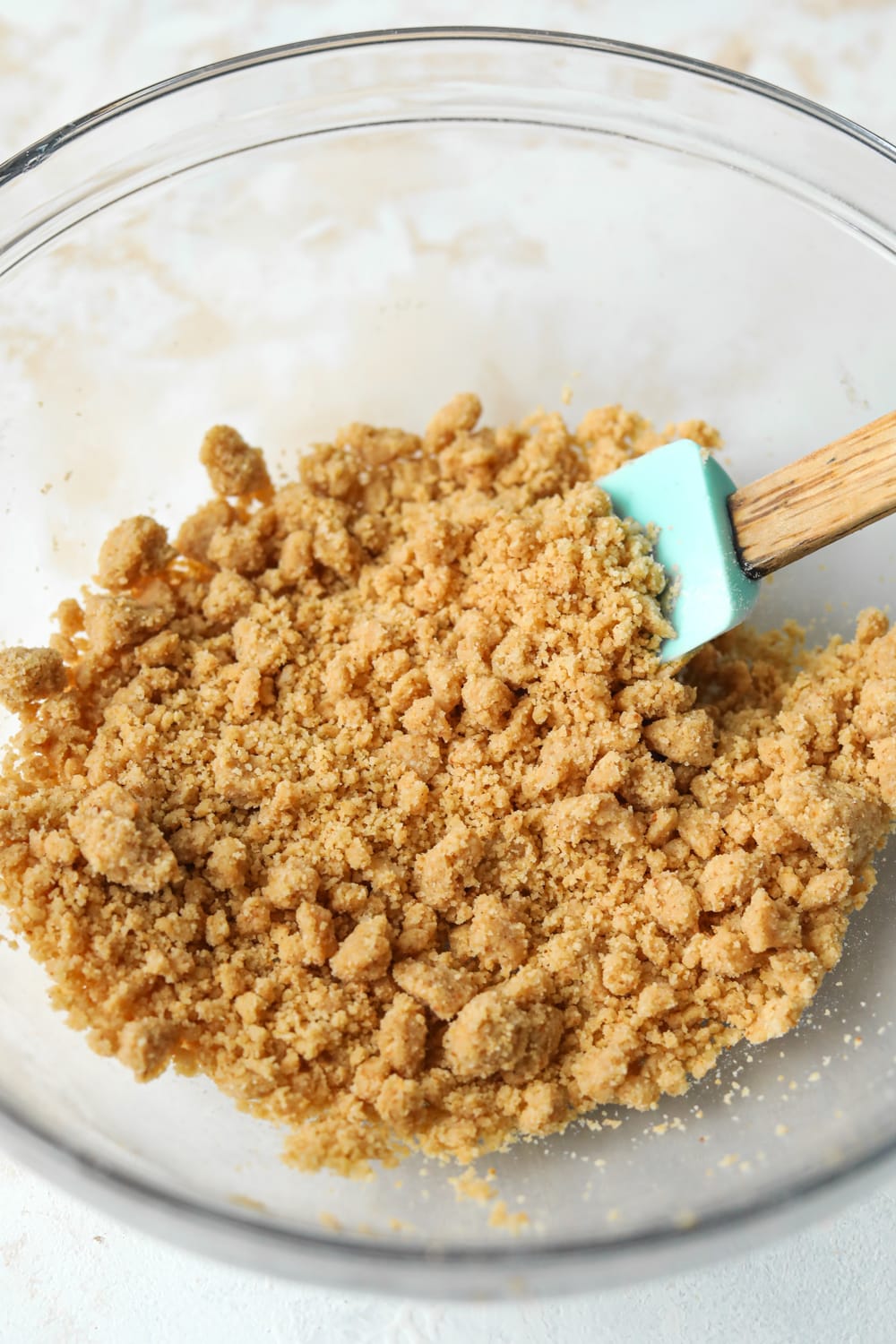 Crumbly dry ingredients in a glass bowl. The bowl is on a white table.