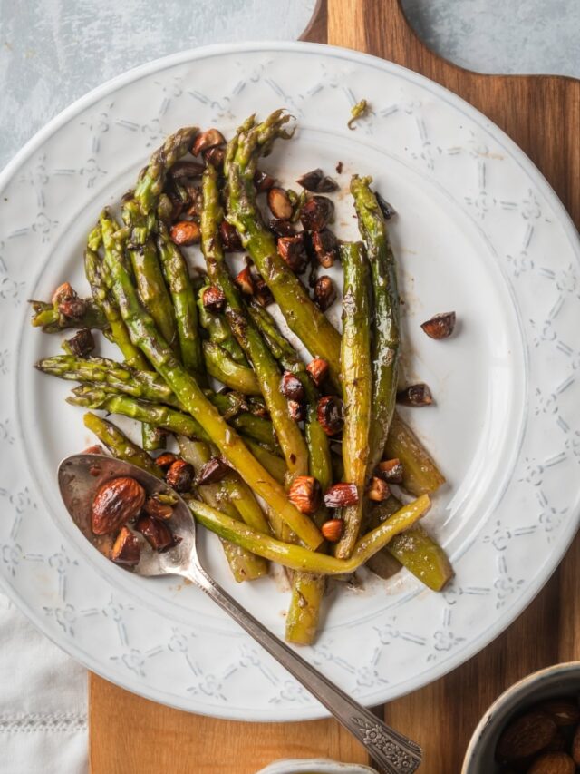 Asparagus and some almonds on top of white plate on part of a wooden cutting board.