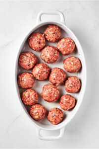 A white baking dish with uncooked meatballs in it.