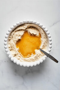 A white bowl filled with almond flour and melted butter in the middle of it.