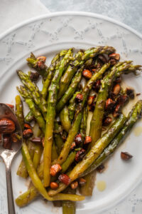 A bunch of asparagus and almonds on top of a white plate.