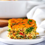 A square of breakfast casserole on top of a white plate on a gray counter.