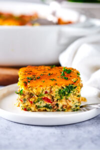 A square of breakfast casserole on top of a white plate on a gray counter.