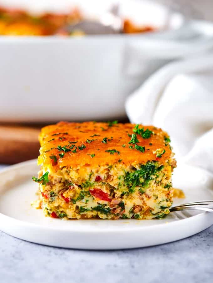 A square of breakfast casserole on top of a white plate on a gray counter.