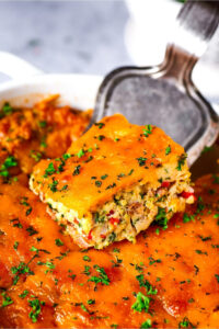 A slice of breakfast casserole been scooped out from the entire casserole from a silver spatula.