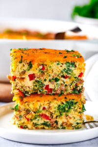 Two squares of breakfast casserole stacked on top of one another on a white plate.