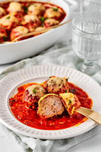 A white plate with three meatballs on it. One meatball is cut in half and a fork is in the ½ of it.