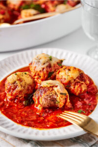 A white plate with four meatballs and tomato sauce on it.