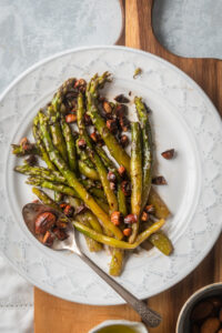 Asparagus and some almonds on top of white plate on part of a wooden cutting board.