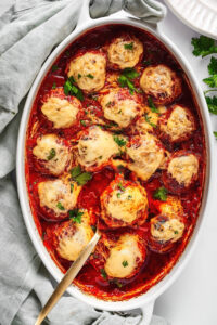 A white baking dish with meatballs covered and tomato sauce and cheese in it.
