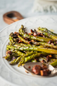 Part of a white plate with asparagus and almonds on it.