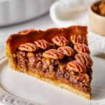 Hey slice of pecan pie on a white plate.