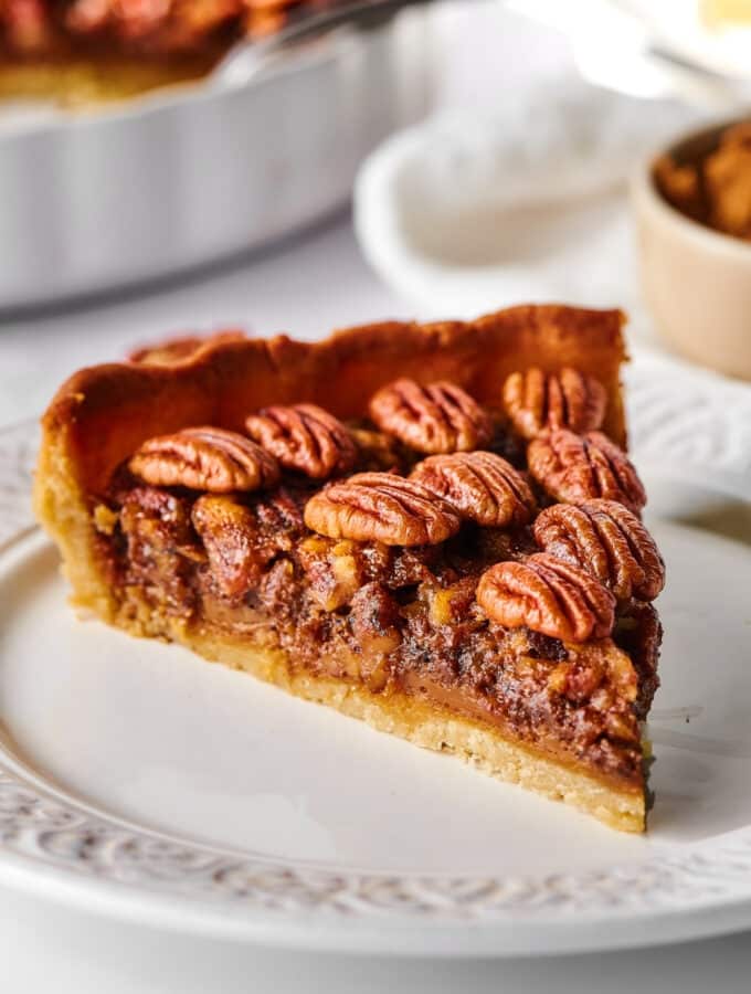 Hey slice of pecan pie on a white plate.