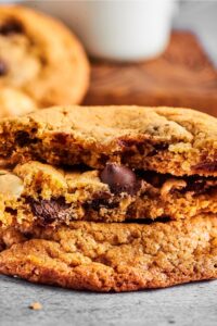 Part of a cookie with part of two chocolate chip cookies on top of it with a bite out of the front of them.