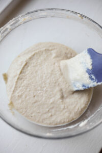 A clear glass bowl filled with batter. There is a blue spatula in the bowl.