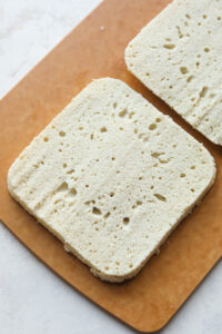 White bread on a tan cutting board. The cutting board is on a white table.