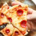 A hand holding a slice of cheese and pepperoni pizza.