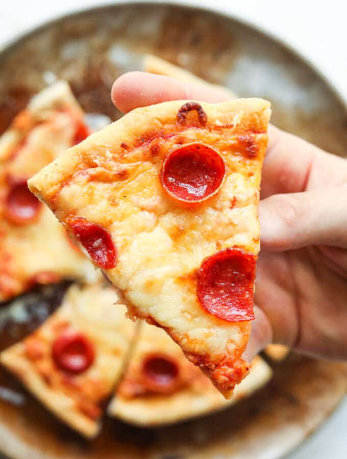 A hand holding a slice of cheese and pepperoni pizza.