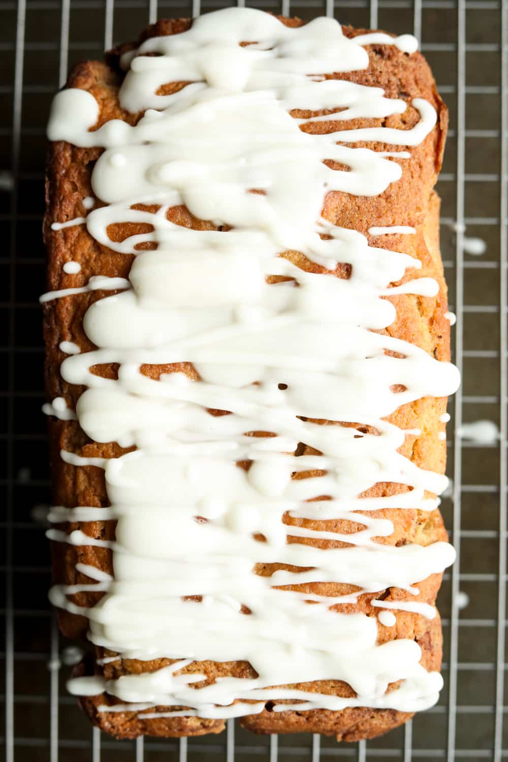 A loaf of cinnamon swirl bread that's been topped with a glaze. The bread is set on a wire drying rack.