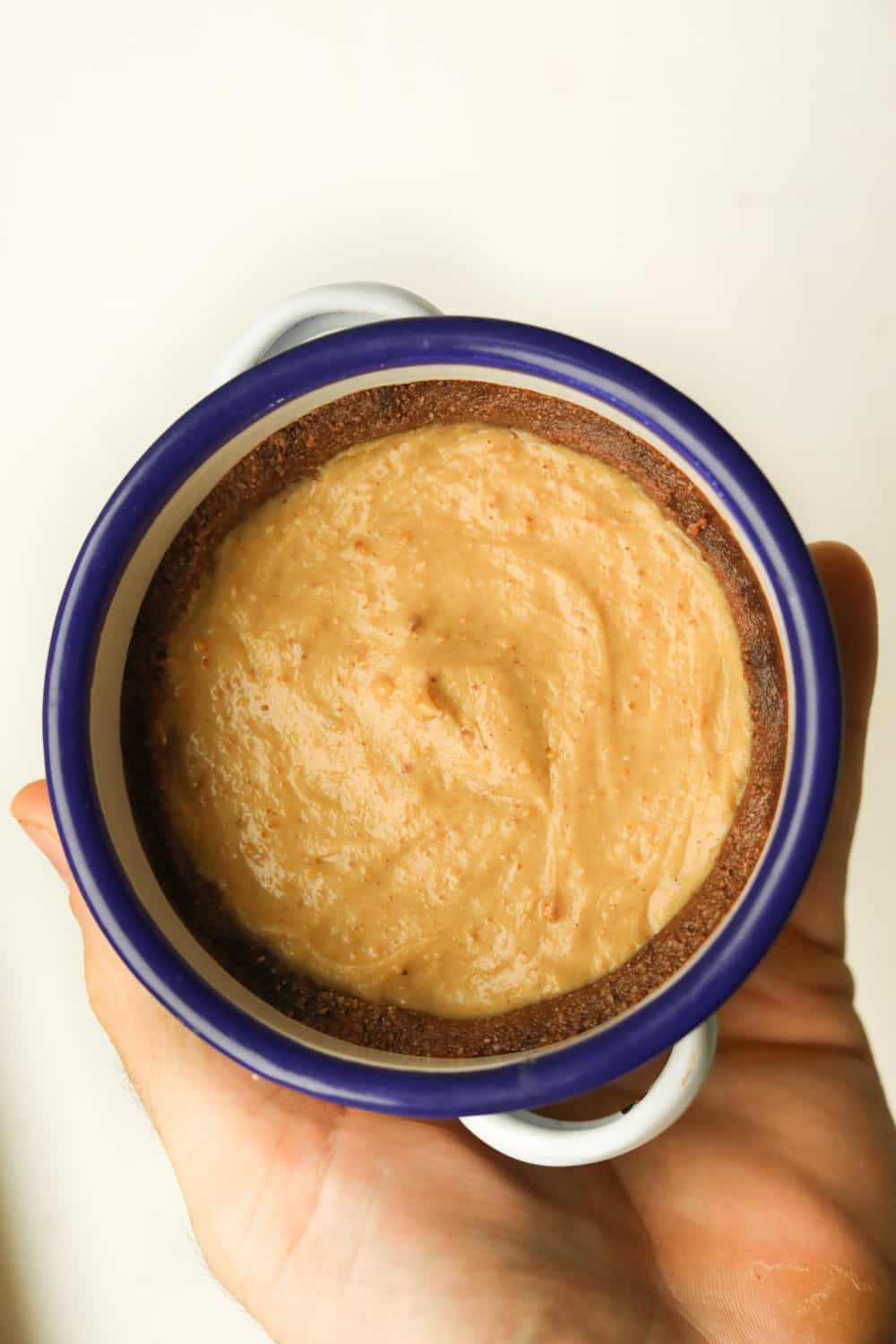 A hand holding a white dish that is filled with a peanut butter pie. The pie has a chocolate crust.