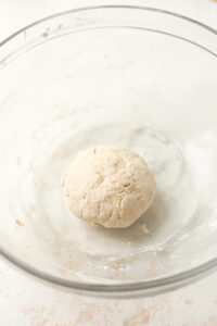 A bowl of pizza dough in a clear bowl.