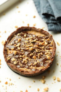 A peanut butter pie with crushed peanuts around it. The pie is set on a white table.