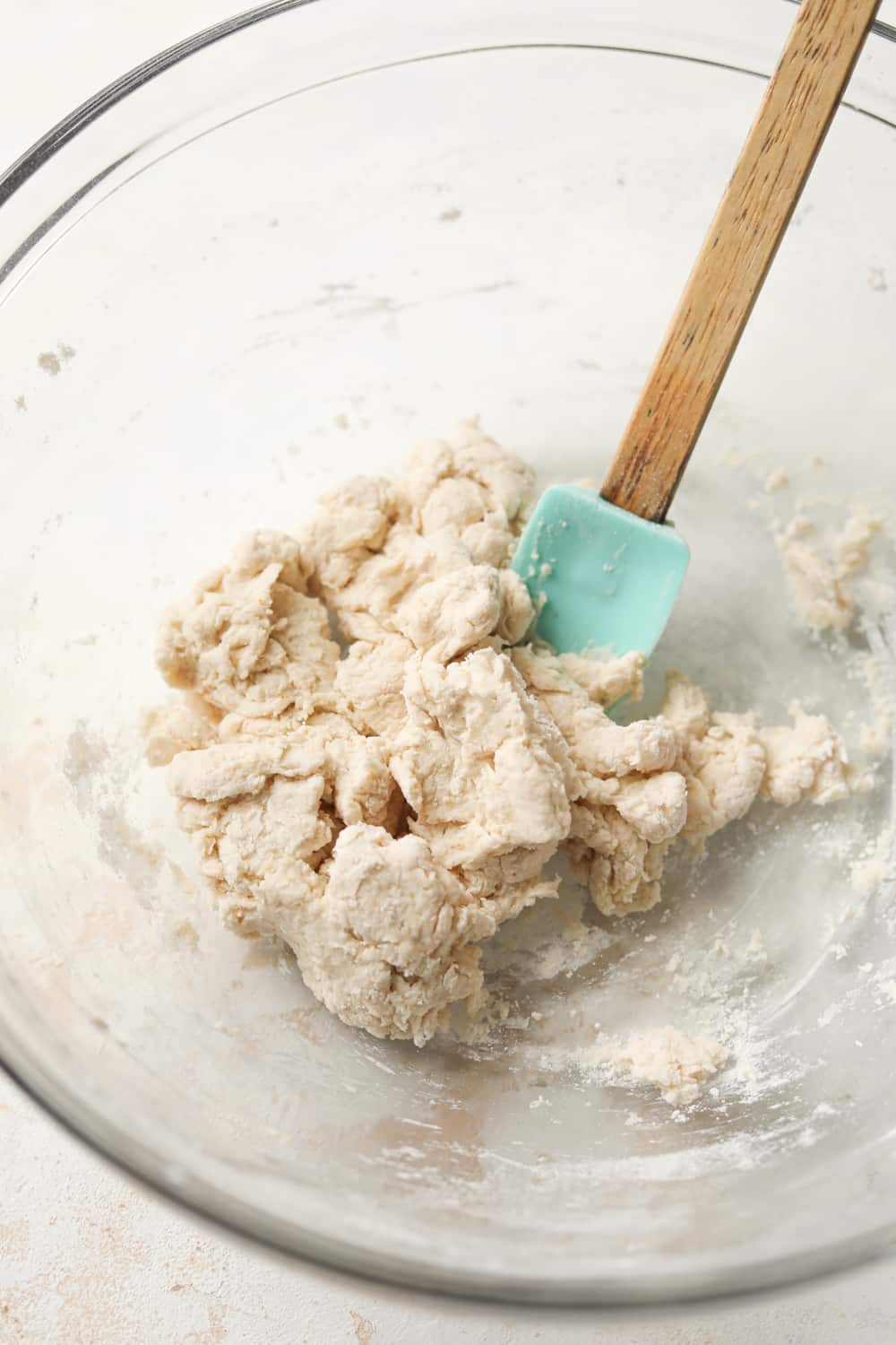 Crumbles of dough in a clear bowl. There's a turquoise bachelor inside of the bowl.