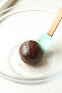 A ball of chocolate dough inside of a glass dish. There is a turquoise spatula inside of the bowl.