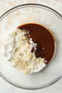 Wet and dry ingredients in a clear glass bowl. The bowl is set on a white table.