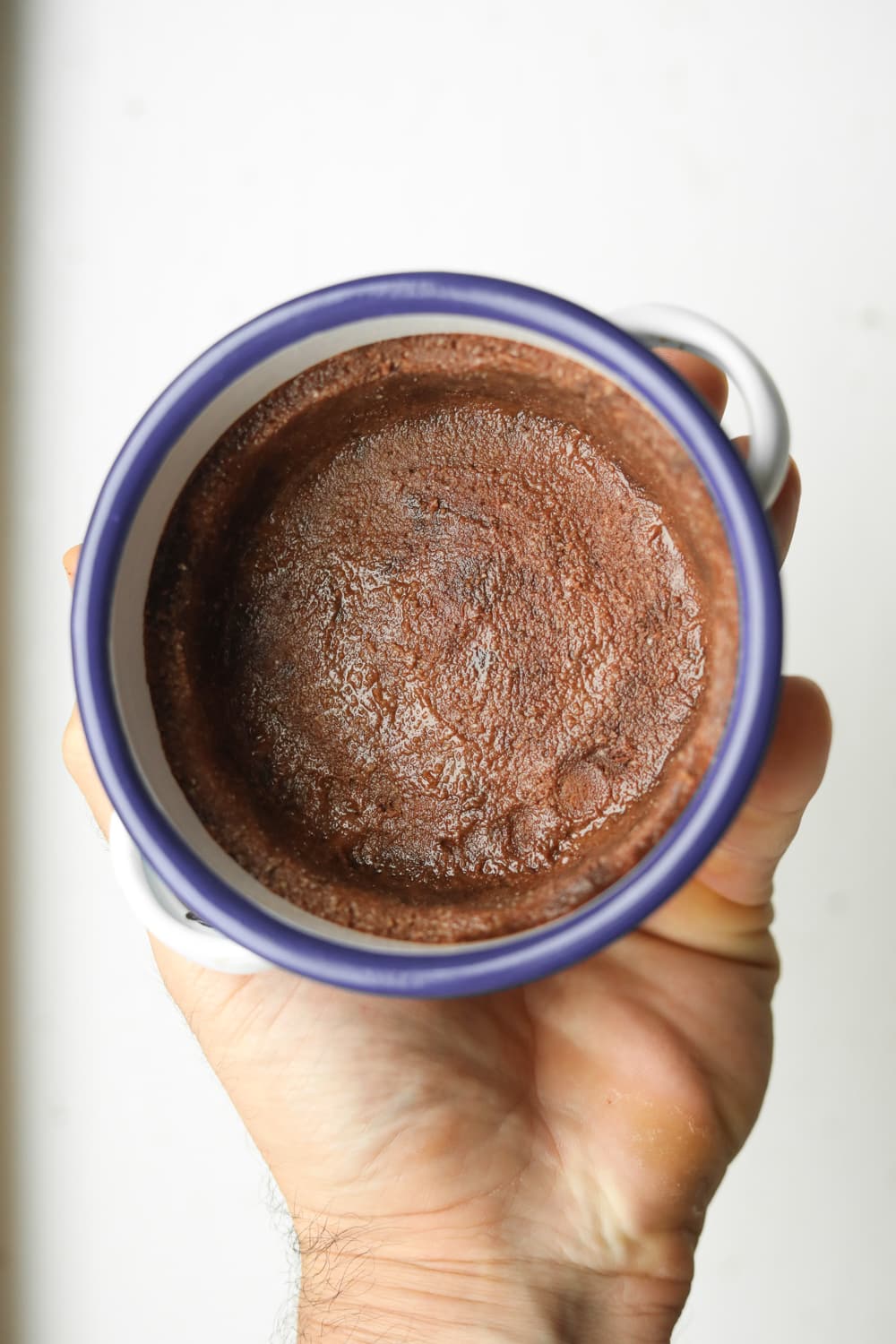 A hand holding a white dish with a blue rim and a chocolate pie crust is inside of the dish.