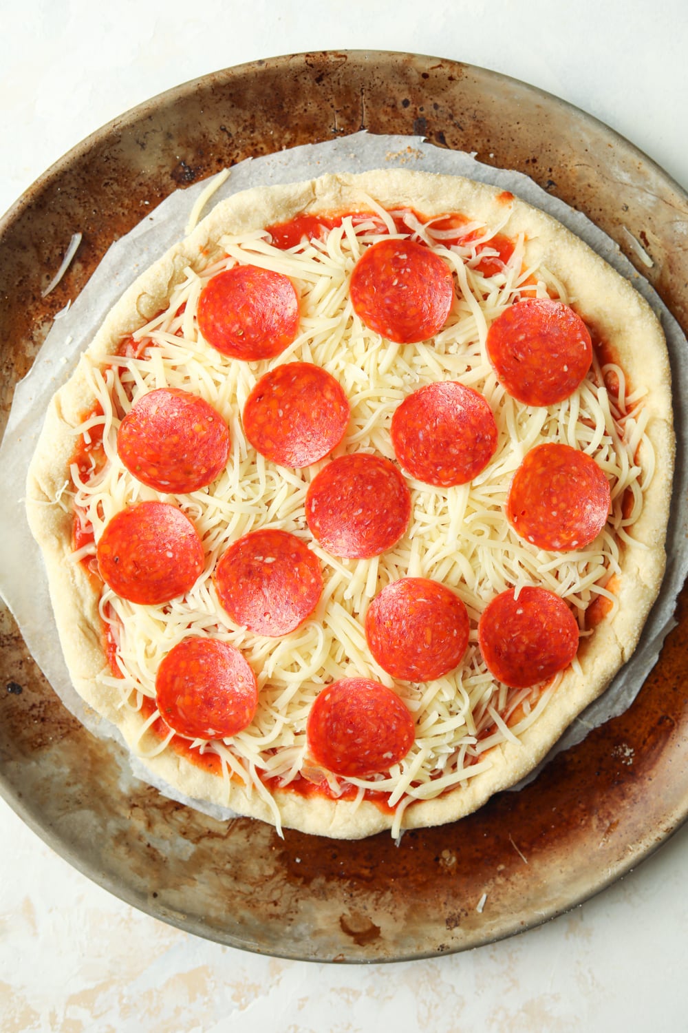 And uncooked cheese and pepperoni pizza on a gray and brown nonstick pizza tray.