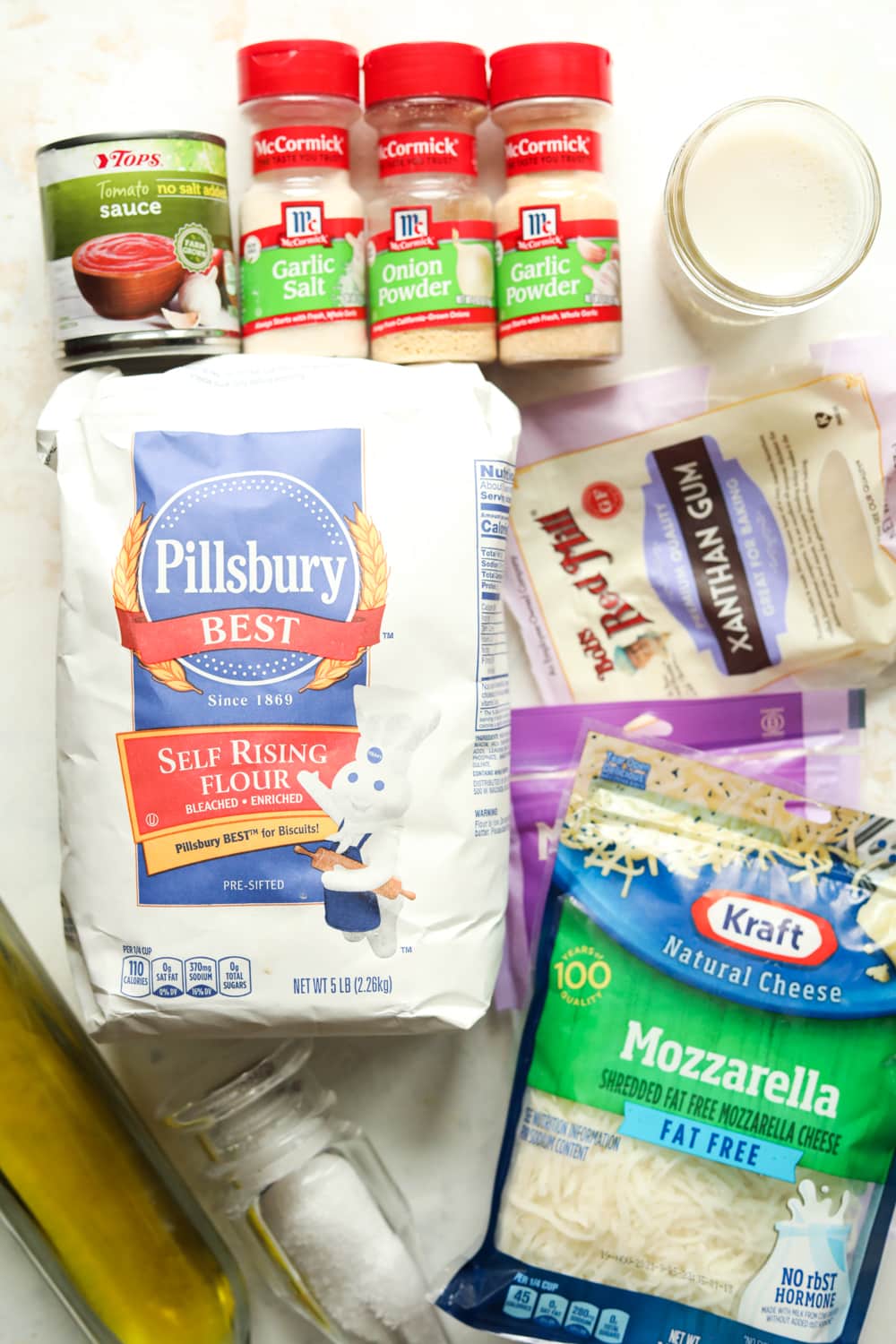 A variety of ingredients to make pizza with set on a white table.