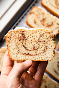 A hand holding a slice of cinnamon swirl bread.