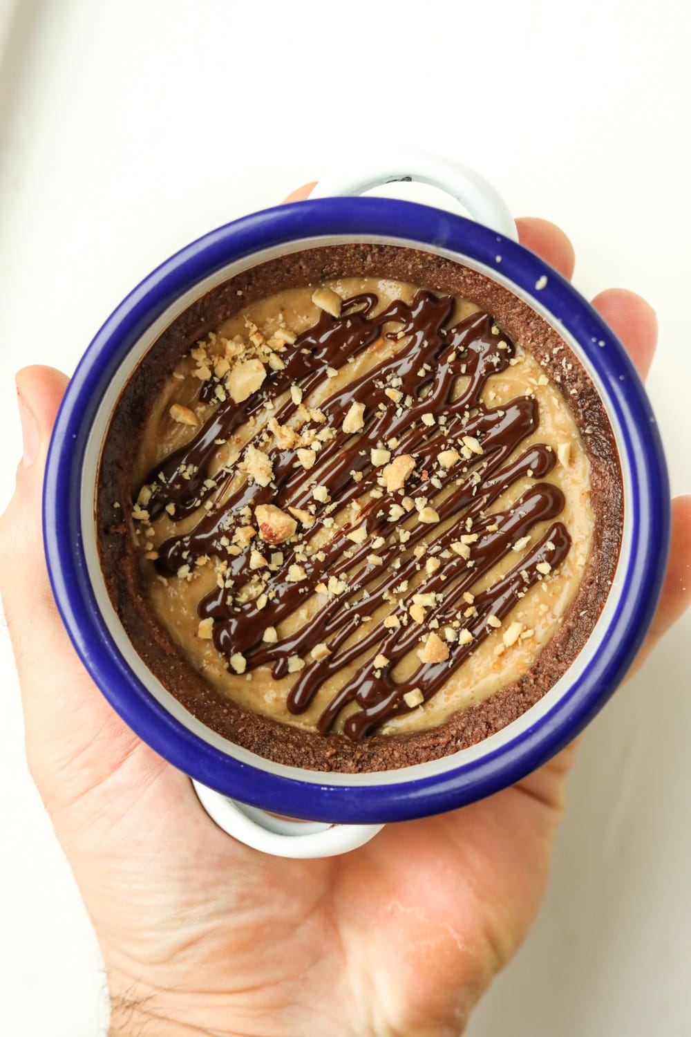 A hand holding a peanut butter pie. The pie is inside a white dish, and it has a blue rim.