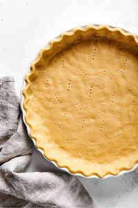 Part of an almond flour pie crust in a white pie dish on a white counter.