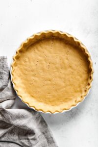 An almond flour pie crust in a white pie dish and a white counter.