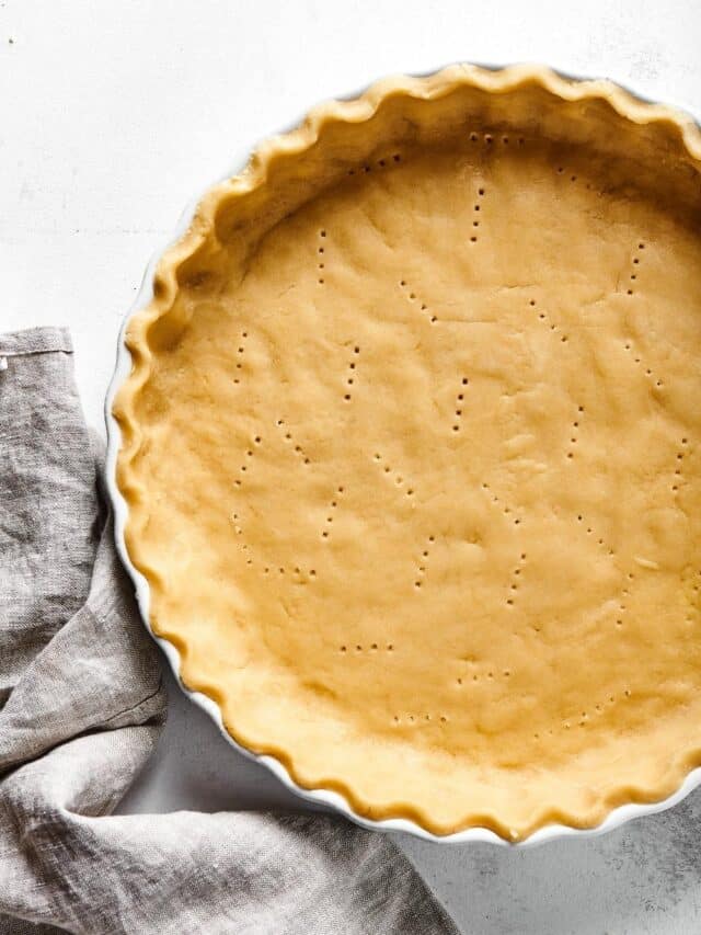 Part of an almond flour pie crust in a white pie dish on a white counter.