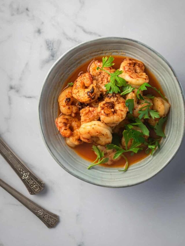 Shrimp in a sauce in a gray bowl on a white counter.