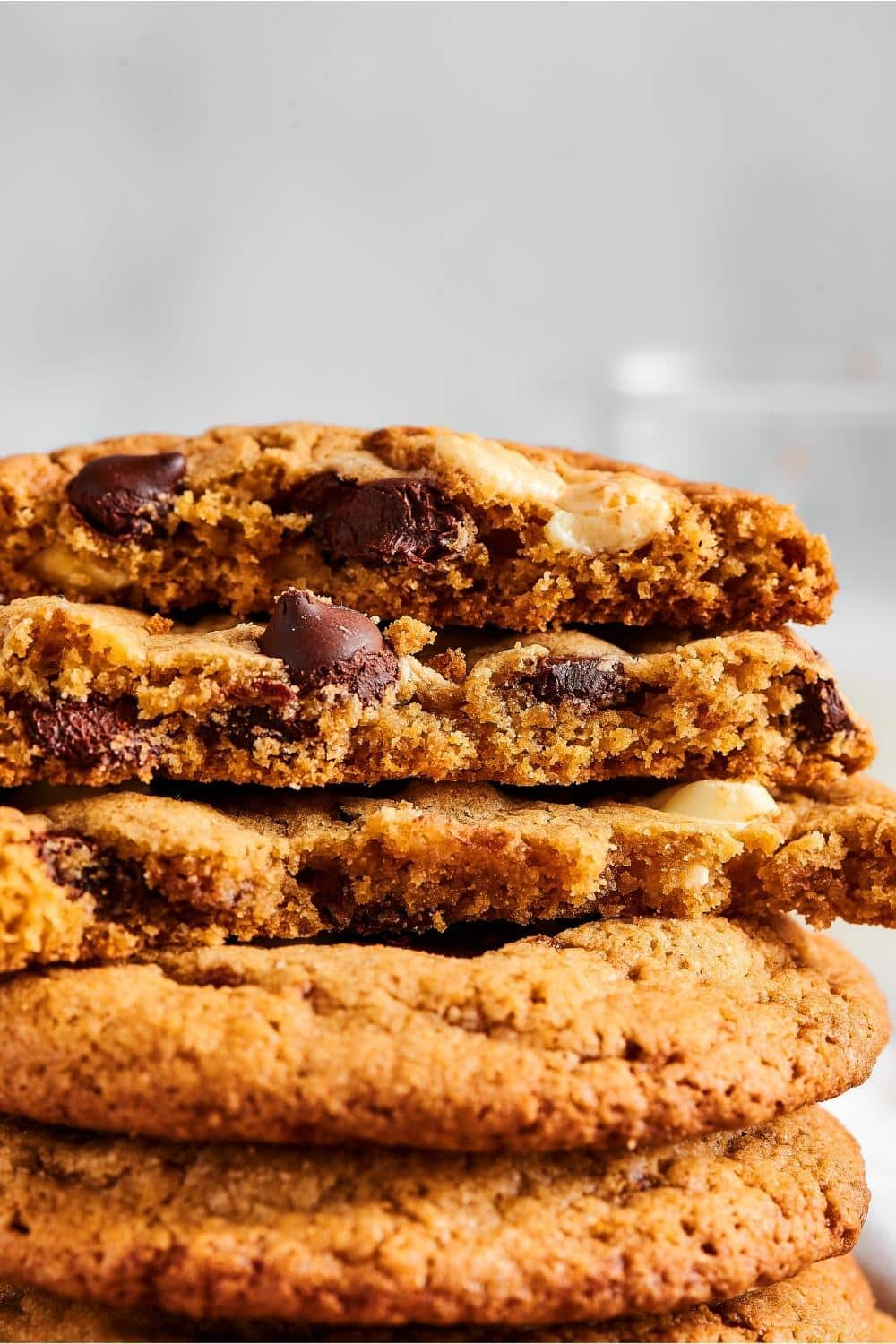 Part of two whole chocolate chip cookies with part of three chocolate chip cookies stacked on top of them. A bite is taken out of the front of the top three cookies.