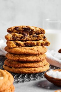 Hey stack of four chocolate chip cookies with three more chocolate chip cookies with a bite out of the front on top of those. All of the cookies are on a wire rack.