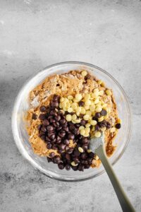 A glass bowl filled with cookie dough with milk and white chocolate chips on top.