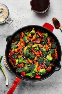 Skillet filled with broccoli, red peppers, and chicken covered in a stir fry sauce with some sesame seeds on top.