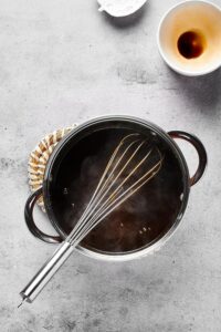 A pot with stirfry sauce in it with a whisk in the pot. Behind it is an empty white ball where the sauce was in.