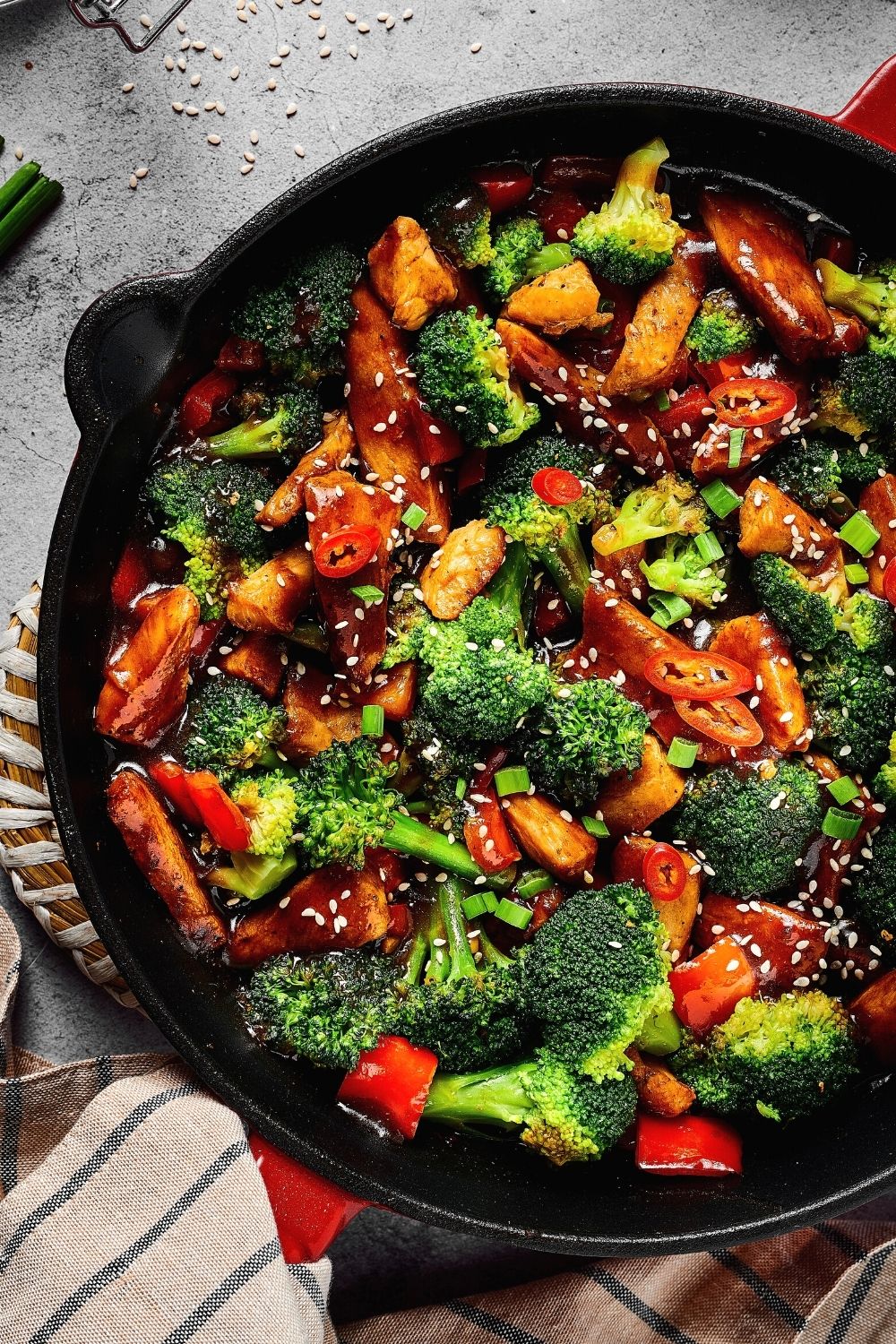 ¾ of a skillet with broccoli, chicken, and red peppers all covered in a stirfry sauce with some sesame seeds on top.