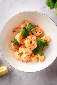 A bunch of shrimp on top of one another in a white bowl on a gray counter.