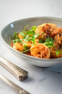 Part of a gray bowl on a white counter that is filled with shrimp.