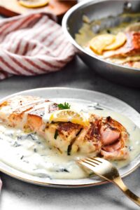 A plate with a salmon fillet caught at the front sitting in a creamy garlic butter sauce.
