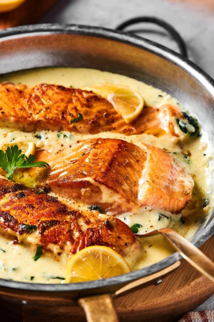 Part of a skillet with three salmon fillets in it sitting in a lemon garlic butter sauce.