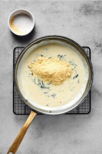 A skillet with creamy garlic butter sauce in it with parmesan cheese on top. The skillet is on a wire rack on a grey counter.