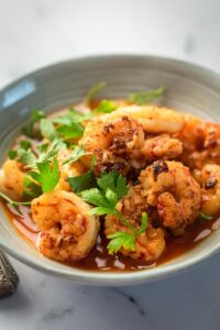 Part of a gray bowl that is filled with some shrimp overlapping one another.